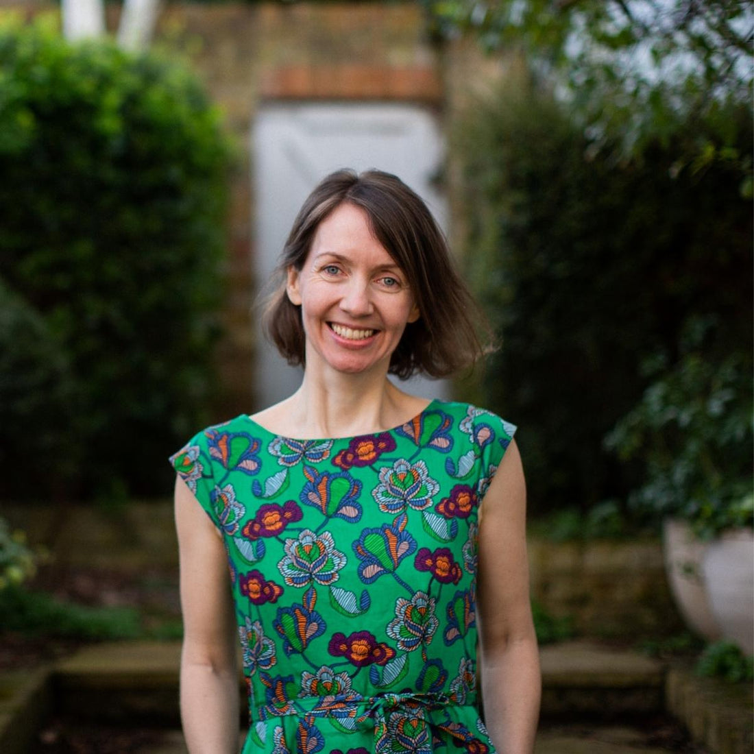 Tara Ghosh, hormone health educator, smiling outdoors in a green floral dress with a blurred garden background.