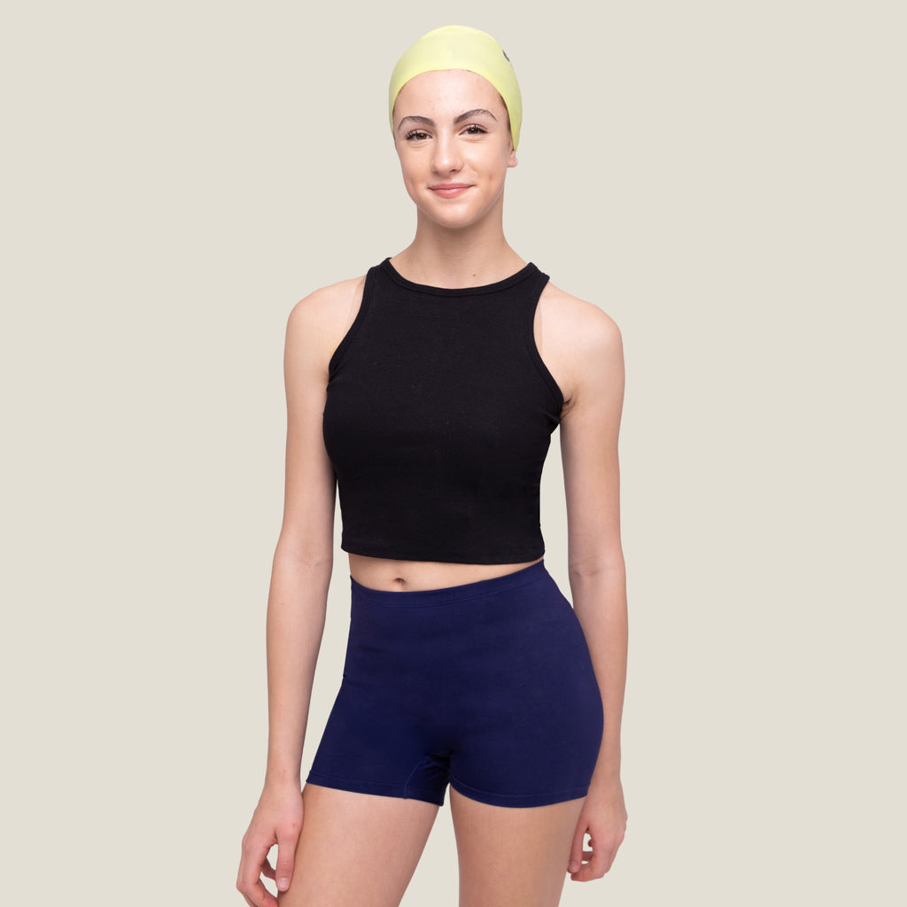 Older Teenage girl wearing a black sleeveless top and navy WUKA swim shorts with a yellow swim cap