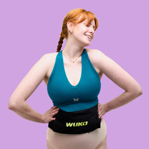 An adult woman smiling and looking relaxed, wearing the WUKA hot water bottle around her waist. For comfort and period pain relief